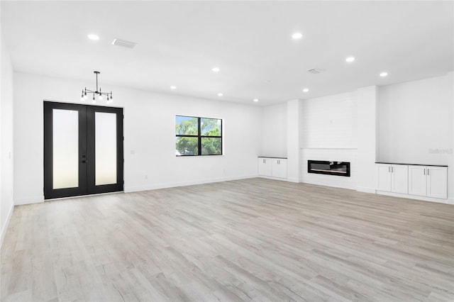 unfurnished living room with brick wall, light hardwood / wood-style floors, a large fireplace, and french doors