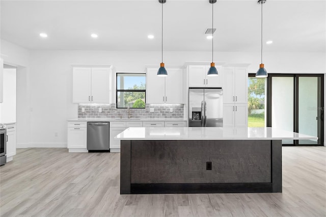 kitchen featuring pendant lighting, tasteful backsplash, white cabinetry, appliances with stainless steel finishes, and light hardwood / wood-style floors