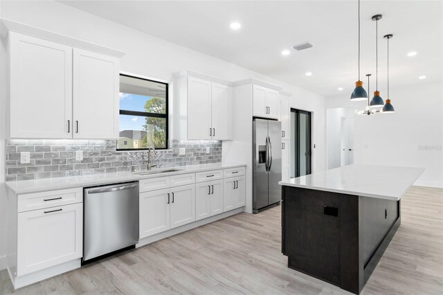 kitchen with appliances with stainless steel finishes, sink, light hardwood / wood-style flooring, and pendant lighting