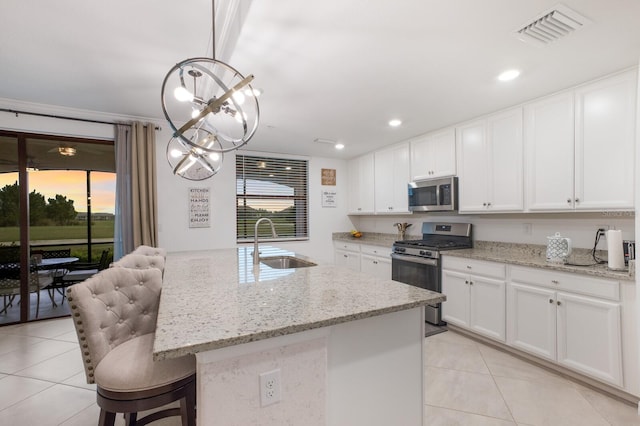 kitchen featuring hanging light fixtures, white cabinets, a center island with sink, and stainless steel appliances