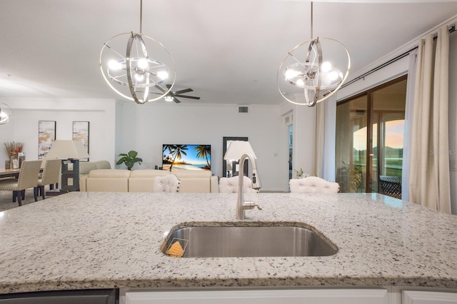 kitchen featuring sink, ornamental molding, light stone counters, and pendant lighting