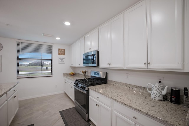 kitchen with appliances with stainless steel finishes, white cabinets, light tile flooring, and light stone counters