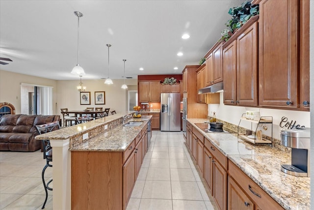 kitchen with decorative light fixtures, light tile patterned flooring, a kitchen bar, a large island with sink, and stainless steel fridge