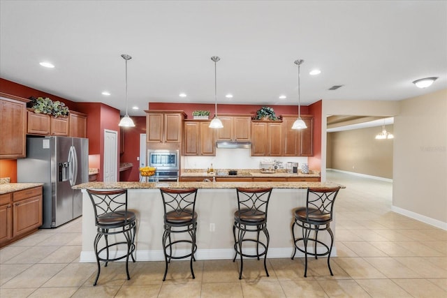 kitchen with a breakfast bar, stainless steel appliances, a kitchen island with sink, and pendant lighting