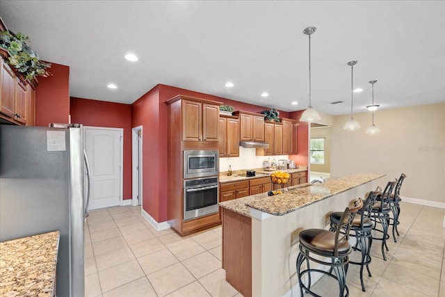 kitchen featuring stainless steel appliances, light stone counters, an island with sink, a breakfast bar area, and hanging light fixtures