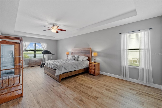 bedroom featuring light wood-type flooring, ceiling fan, and a tray ceiling