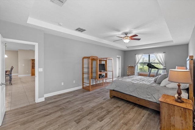 bedroom with a raised ceiling, ceiling fan, and light hardwood / wood-style floors