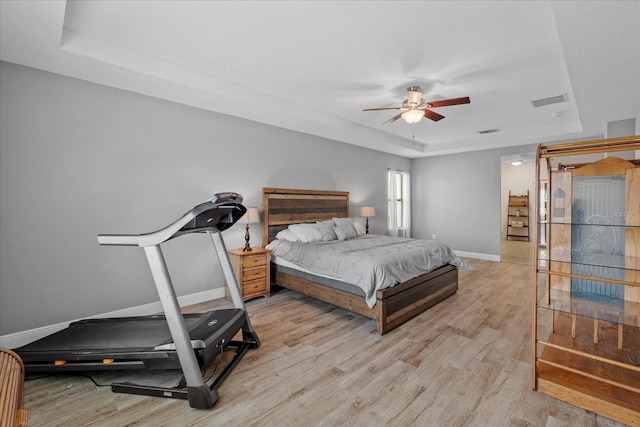 bedroom featuring ceiling fan, a tray ceiling, and light hardwood / wood-style floors