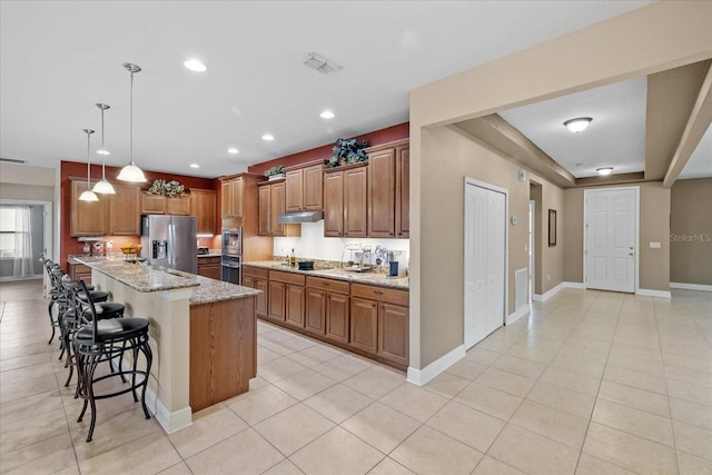 kitchen featuring stainless steel appliances, pendant lighting, an island with sink, light stone countertops, and a breakfast bar