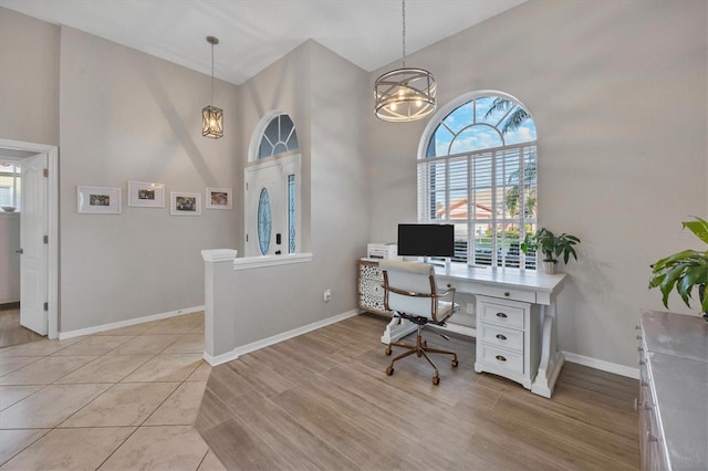 home office with a high ceiling, a notable chandelier, and light tile floors