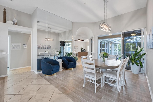 dining area featuring a high ceiling, plenty of natural light, ceiling fan with notable chandelier, and light hardwood / wood-style flooring