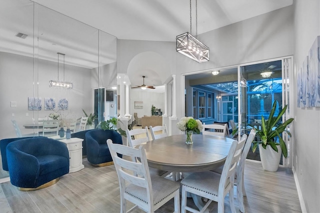 dining space with a towering ceiling, hardwood / wood-style flooring, and ceiling fan with notable chandelier