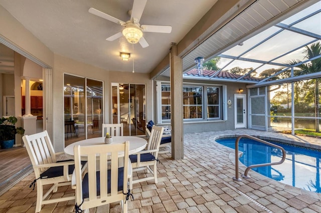 pool at dusk featuring a patio, glass enclosure, and ceiling fan