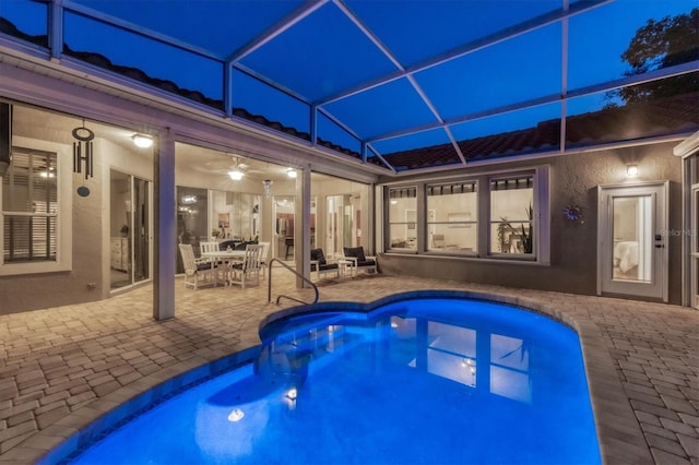 pool at twilight featuring ceiling fan, glass enclosure, and a patio