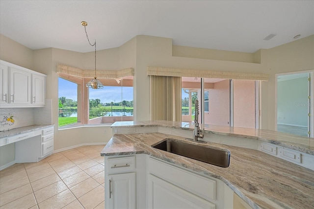 kitchen featuring a water view, sink, light stone countertops, decorative light fixtures, and white cabinetry