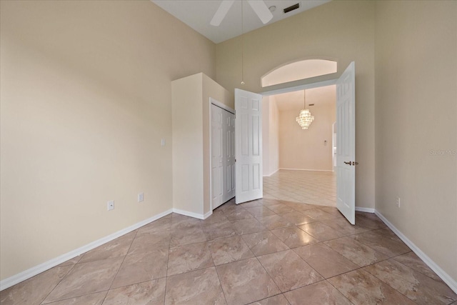 empty room featuring a high ceiling, ceiling fan with notable chandelier, and light tile patterned flooring