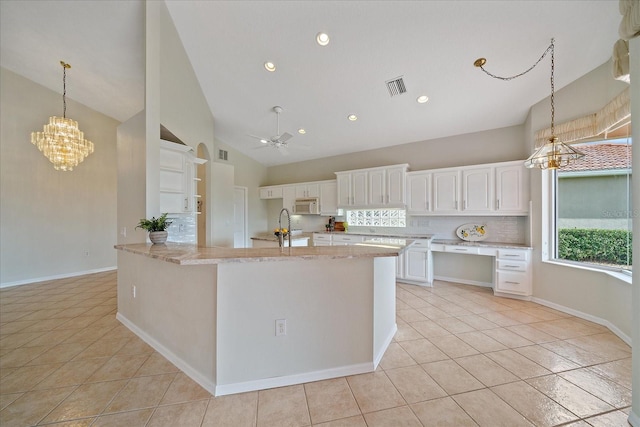 kitchen with light stone countertops, tasteful backsplash, ceiling fan with notable chandelier, light tile patterned floors, and white cabinets