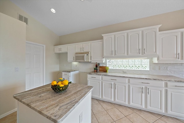 kitchen with lofted ceiling, light tile patterned floors, white cabinetry, backsplash, and a kitchen island