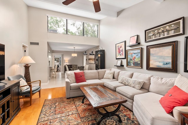 living room with beam ceiling, light hardwood / wood-style flooring, ceiling fan, and a high ceiling