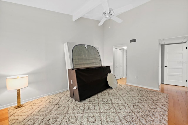 bedroom featuring ceiling fan, beamed ceiling, light hardwood / wood-style floors, and a high ceiling