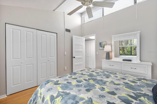 bedroom featuring ceiling fan, light wood-type flooring, a high ceiling, and a closet