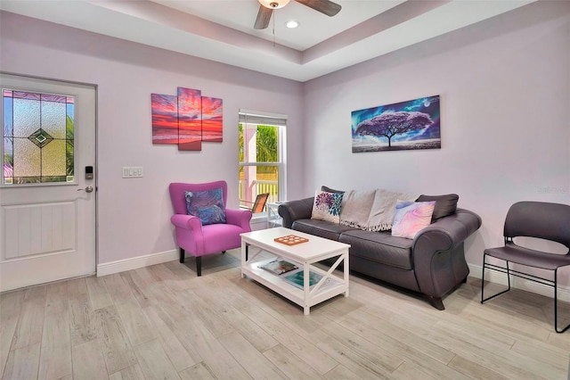 living room featuring ceiling fan, a raised ceiling, and light hardwood / wood-style flooring