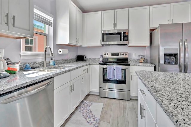 kitchen with appliances with stainless steel finishes, sink, white cabinets, and light stone countertops