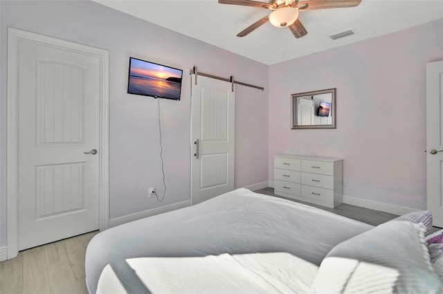 bedroom with a barn door, ceiling fan, and light hardwood / wood-style floors