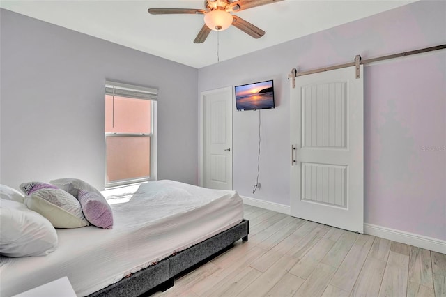 bedroom with a barn door, ceiling fan, and light hardwood / wood-style flooring