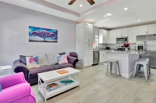 living room featuring ceiling fan, sink, light hardwood / wood-style flooring, and a raised ceiling