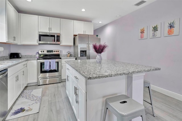 kitchen with light hardwood / wood-style flooring, a kitchen island, a kitchen bar, and stainless steel appliances