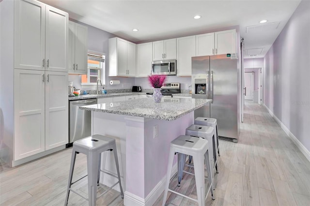 kitchen with a center island, light wood-type flooring, appliances with stainless steel finishes, white cabinets, and a kitchen bar