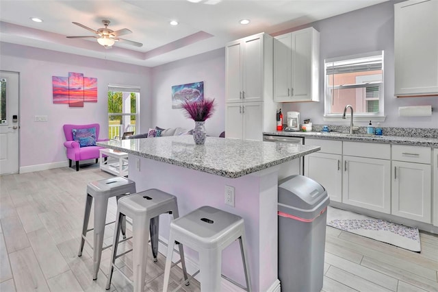 kitchen with ceiling fan, light hardwood / wood-style floors, a tray ceiling, white cabinets, and a kitchen bar