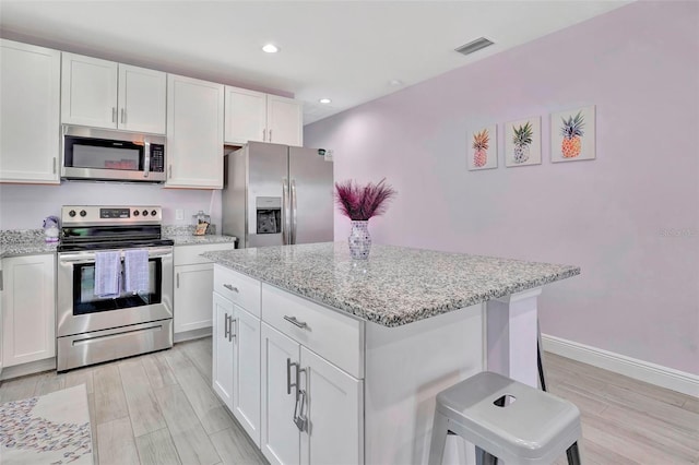 kitchen featuring a center island, stainless steel appliances, white cabinets, and light wood-type flooring