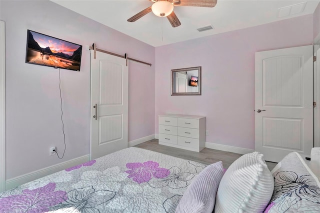 bedroom featuring ceiling fan, a barn door, and light hardwood / wood-style flooring