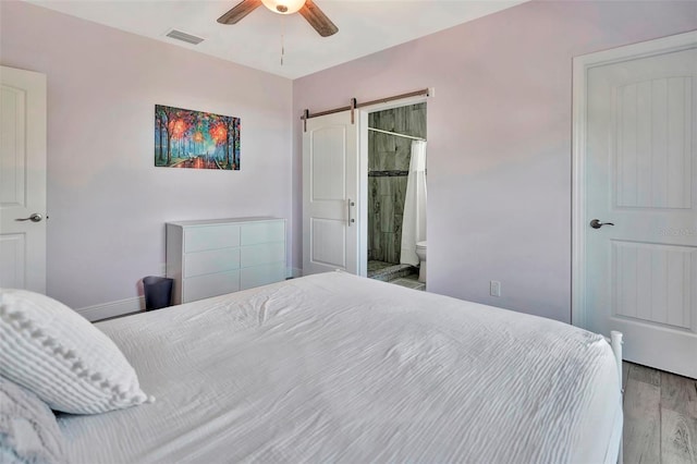 bedroom with a barn door, ceiling fan, ensuite bath, and wood-type flooring