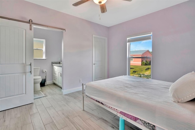 bedroom with a barn door, connected bathroom, ceiling fan, and light hardwood / wood-style flooring