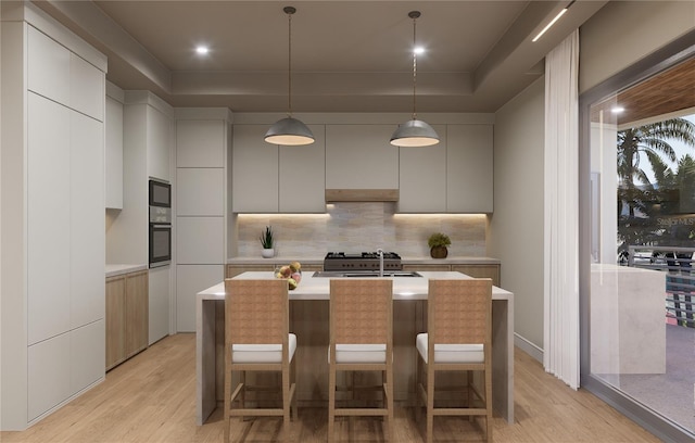 kitchen with black microwave, sink, wall oven, light hardwood / wood-style floors, and a tray ceiling