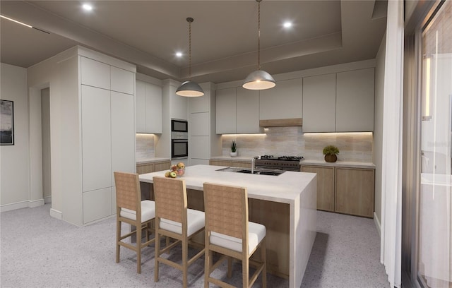 kitchen with black microwave, a raised ceiling, wall oven, pendant lighting, and a kitchen island with sink