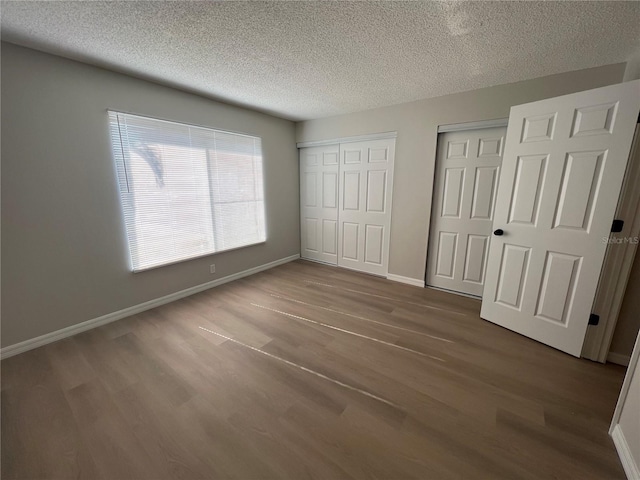 unfurnished bedroom with two closets, a textured ceiling, and dark wood-type flooring