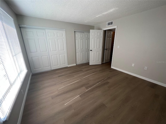 unfurnished bedroom featuring multiple closets, dark wood-type flooring, multiple windows, and a textured ceiling