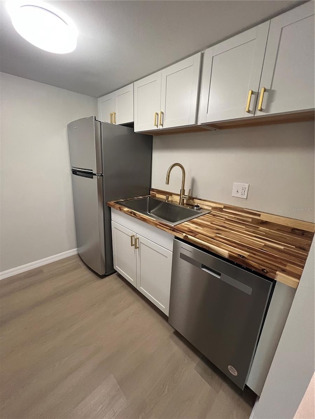 kitchen featuring white cabinets, butcher block countertops, appliances with stainless steel finishes, and light hardwood / wood-style floors