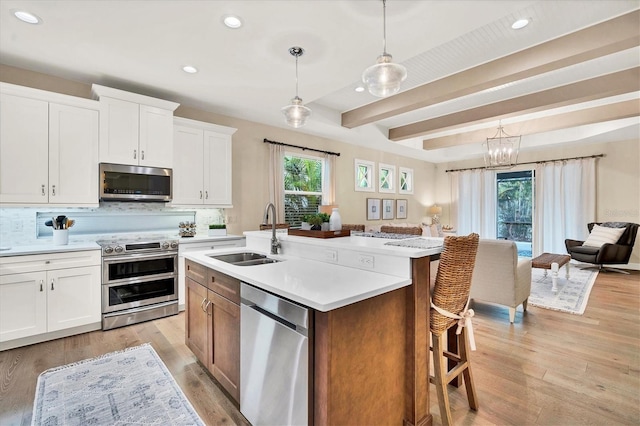 kitchen with pendant lighting, a kitchen island with sink, sink, appliances with stainless steel finishes, and white cabinetry