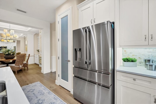 kitchen featuring white cabinetry, light hardwood / wood-style flooring, a notable chandelier, stainless steel fridge, and decorative backsplash