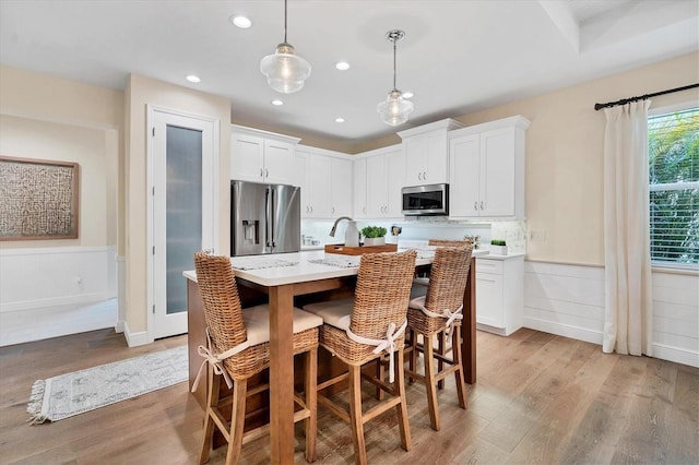 kitchen with a kitchen bar, appliances with stainless steel finishes, decorative light fixtures, light hardwood / wood-style flooring, and white cabinetry