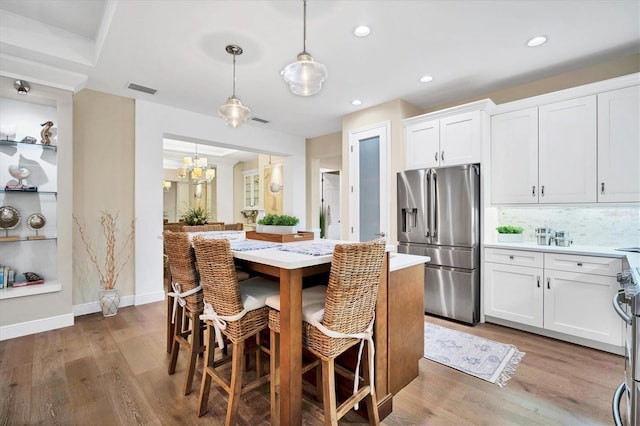 kitchen with light hardwood / wood-style floors, white cabinets, pendant lighting, and appliances with stainless steel finishes