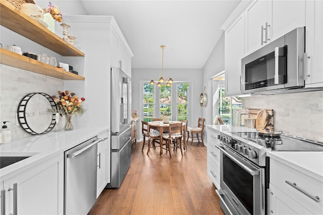 kitchen with lofted ceiling, premium appliances, hardwood / wood-style flooring, decorative light fixtures, and tasteful backsplash