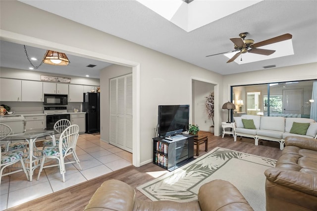 tiled living room featuring ceiling fan, a textured ceiling, and a skylight