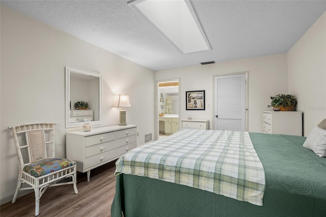 bedroom featuring hardwood / wood-style floors, connected bathroom, a textured ceiling, and a skylight