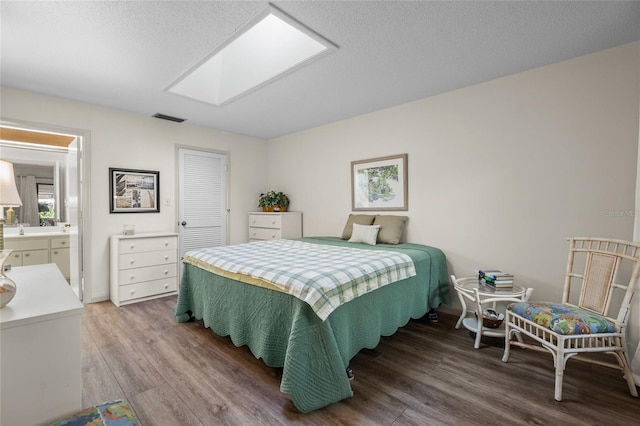 bedroom featuring ensuite bathroom, a skylight, and hardwood / wood-style floors